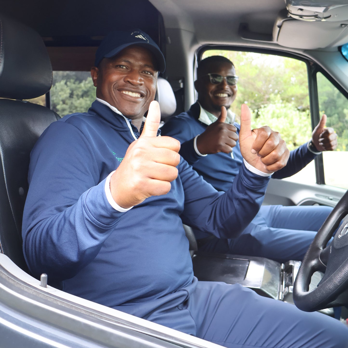 Two men in a vehicle, one pointing out of the window with a smile.