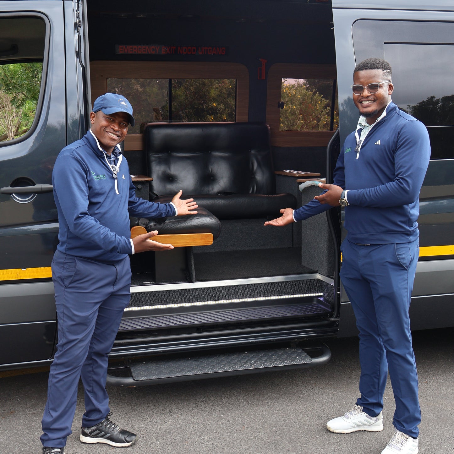 Two men in blue uniforms standing next to a black van with open doors.