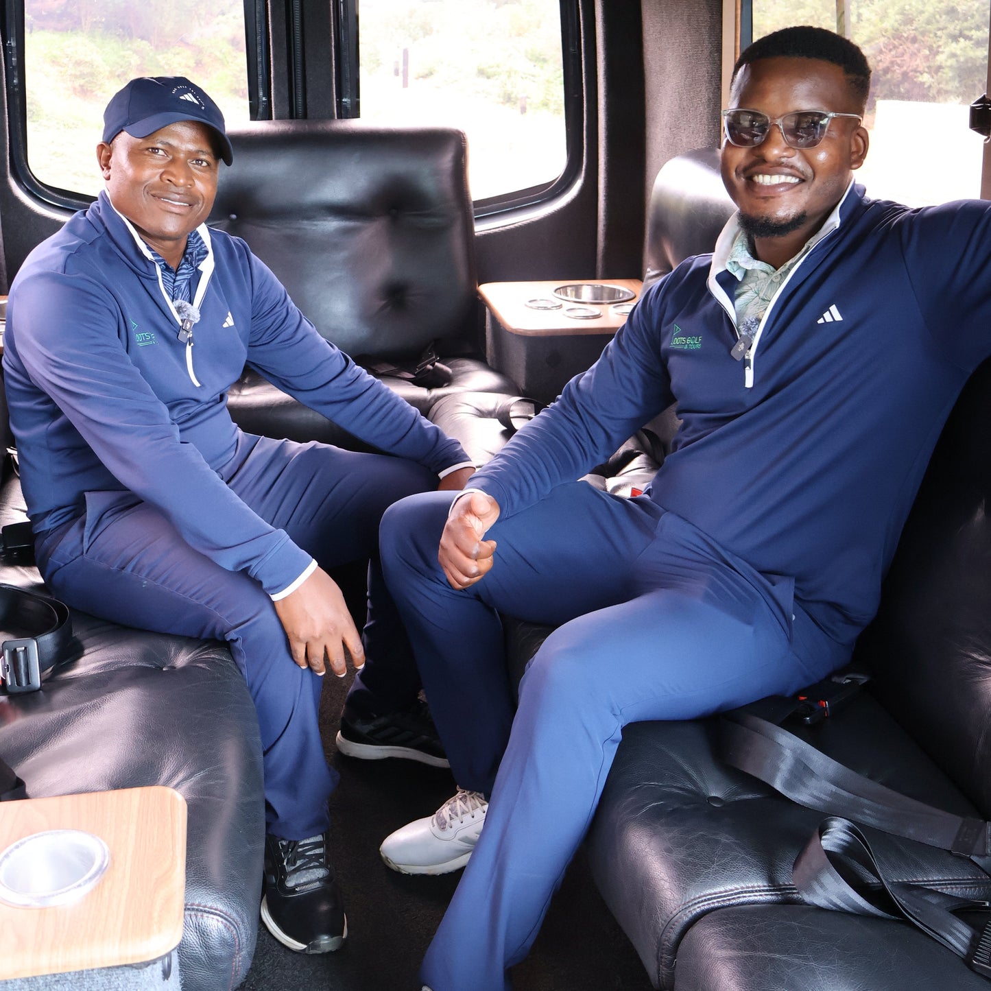 Two men in matching blue tracksuits sitting inside a vehicle.